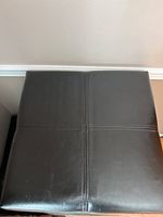 Top view of black leather-like ottoman showing cross-stitched seams and smooth surface