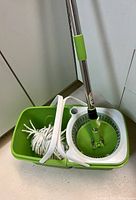 Photo showing mop inserted in spin mechanism of green plastic dual compartment bucket. White twisted mop head is detachable.