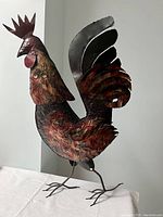 Full view of the metal rooster ornament showing the body, head, and legs with painted colors and embossed details.