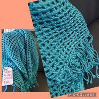 Photo showing the full view of the turquoise knitted shawl draped on a surface, highlighting the mesh pattern and fringed edges.