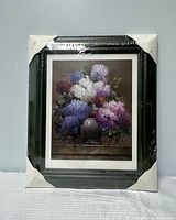 Front view of framed print showing lilacs in a vase with light brown background, wrapped in plastic and with corner protectors.