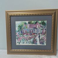 Full view of framed watercolor showing cottage with surrounding flowers and white picket fence.