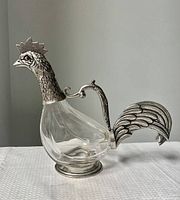 Full side profile of the vintage decanter showing clear glass body shaped as rooster and silver-tone metal head, handle, and tail.
