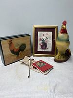 Photo of all items in lot showing the ceramic rooster piggy bank, wooden decorative boxes, framed floral print, carved pipe, and red book, arranged on a white cloth background.