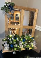Front view of the wood-framed mirror with Christmas decorations of snowmen, blue and silver ornaments, silver ribbons, green garland and battery blue lights.