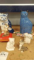 Group photo of seven ceramic cat figurines of various sizes and colors on table surface.