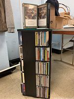 Photo showing a revolving black pressed wood CD holder with glass top, containing classical music CDs arranged on shelves visible on one side.