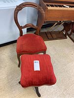 Carved wood chair with red velvet seat cushion and matching foot stool with red velvet cushion and wood base.