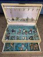 Image showing open vintage jewelry box with assorted ice skating themed pins, earrings, and bracelet distributed in velvet-lined compartments and satin-lined lid holder.