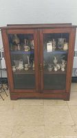 Front view of wood display cabinet with glass doors showing items inside and overall condition.