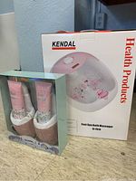 Boxed Kendal Foot Spa Bath Massager model SI-FB10 next to boxed slipper set with foot care products on countertop.