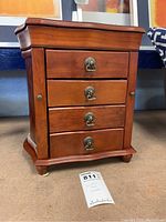 Front view of the wood jewelry box cabinet showing four drawers with metal handles, curved base, and small feet.