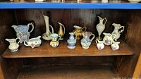 Shelf with twelve miniature pitchers including a pitcher shaped like an armchair, a gold-toned pitcher, and others with floral patterns