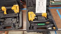 Two yellow and black pneumatic tools inside their plastic cases on a table, including the Bostich model SX150-1 pneumatic nailer and SB-1664FN brad stapler with an instruction manual visible.