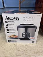 Box front showing Aroma logo, picture of rice cooker, and phrases in Spanish indicating the product is a rice cooker and steamer.
