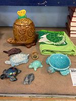 Overview of all turtle-themed items including ceramic figurines, cookie jar, pot holders, and towel on display table.