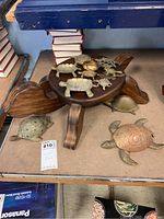 Wooden turtle step stool and six metal/brass turtle figurines arranged on a shelf showing top and front details.