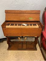 Full front view of vintage wooden Estey organ showing keyboard and pedals on base with worn wood finish.