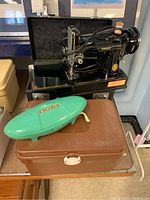 Black Singer sewing machine in brown carry case with teal buttonholer case on top