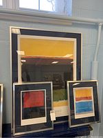 Framed large Mark Rothko print with two smaller framed abstract prints, navy mats and silver frames, arranged near window.