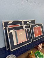Four framed Mark Rothko prints leaning against a blue wall with silver frames and dark navy blue mats.