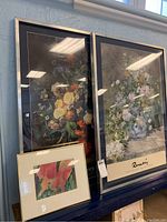 Large and small framed floral posters with silver frames and navy mats, seen near window with sunlight reflections on glass.