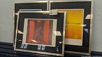 Three framed Mark Rothko prints stacked: red-purple front, yellow center, dark blue rear.