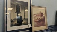 Two framed art prints leaning against wall. One signed Charles Sheeler print, second nautical scene print. Both framed under glass.