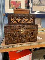 Photo showing the three wooden boxes stacked: the small turtle box on top, a rectangular box with geometric carvings in the middle, and a curved chest with carved figures on the bottom, placed on a wooden surface.