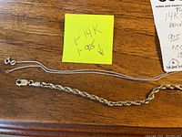 Two sterling silver chains and one gold rope bracelet laid on wooden surface with yellow note indicating markings