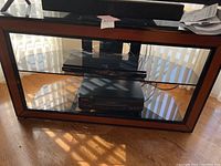 Front view of glass and wood AV stand showing wood frame and glass shelves. Electronics placed on shelves (not included).