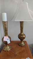 View of matching etched brass table lamp with fabric shade and tall etched brass vase side by side on a wood table.
