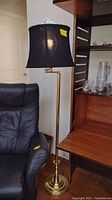 Full view of brass floor lamp with black fabric lampshade next to a chair and wooden desk.