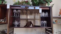 Full view of shelves within wooden cabinet holding crystal drinkware set