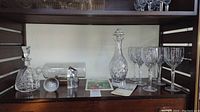 Full view of shelf with two decanters (one Waterford), spherical paperweight, miniature decanter, Cutty Sark ship in a bottle, and six Waterford water goblets