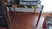End table viewed from the front and side showing brass frame, legs, and clear glass top.