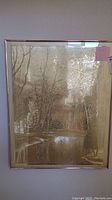 Frontal view of the framed metallic gold forest and stream poster hanging on a wall.