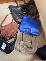 Photo of five leather purses arranged on carpet floor, showing variety in color and style