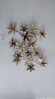 Metal leaf wall art sculpture, showing multiple gold-toned leaves attached to metal stems against a white wall.
