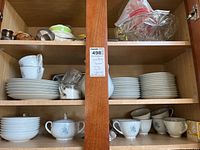 Cabinet shelf showing all the dishware, stacked plates, bowls, cups and a sugar bowl in Noritake Hyannis pattern.