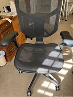 Front view of black mesh office chair showing mesh seat and backrest, padded armrests, and wheeled legs.