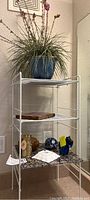 White metal 3-shelf unit with removable marble top and items placed on shelves including faux plant and glass figurines