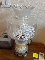 Full view of one hurricane-style table lamp showing frosted glass with floral patterns and glass shade with ruffled edges.