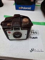 Angled view of the vintage Kodak Brownie Holiday camera showing the film advance knob, lens, and strap.