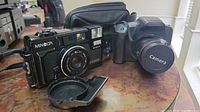 Both cameras displayed side by side with lens cap and black carrying case visible.