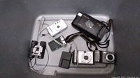 Overview photo showing all items in the lot laid out including cameras, charger, and binoculars.