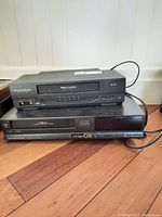 Top view of Durabrand DCV203 VHS player stacked on Electrohome HVRG91 VHS player showing front controls and condition.