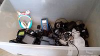 Plastic bin containing assorted electronics including novelty headphones with dog ears, multiple black security cameras, electronic devices, and assorted cables.