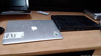 Two laptops on a wooden surface: silver MacBook Air A1456 and a black Lenovo laptop showing damage