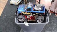 Two photos of a blue and black Nee Bright remote control truck with flame decals, large off-road tires, chrome rims and engine detail sitting in a grey storage bin.